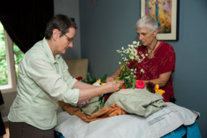 Two women placing flowers on a shrouded body for a home funeral.